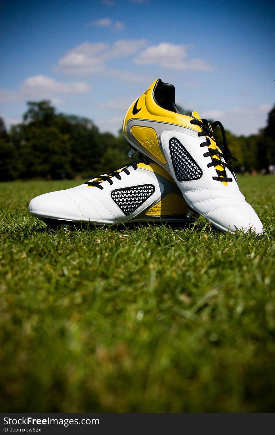 Closeup of designer sports shoes in yellow, black and white colors placed artistically on grass with selective focus.