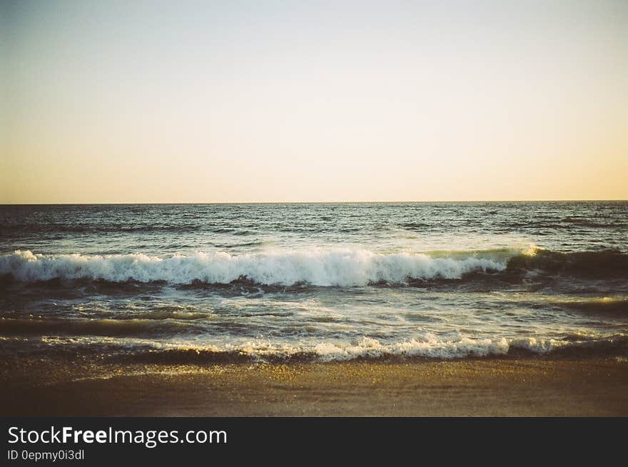 Waves and foam seen from a sandy beach as the tide comes in, pale blue gray sky. Waves and foam seen from a sandy beach as the tide comes in, pale blue gray sky.