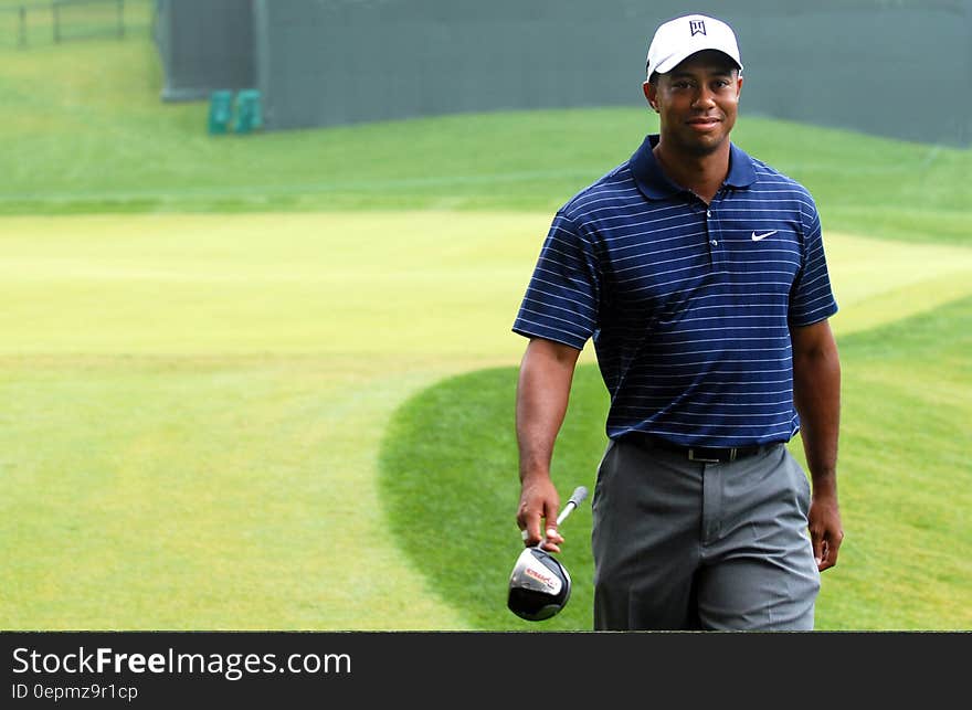 Tiger Woods walking in golf course carrying club. Tiger Woods walking in golf course carrying club.