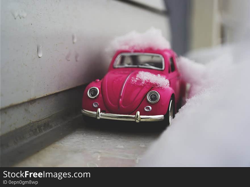 Close up of toy pink Beetle car covered in snow next to exterior wall. Close up of toy pink Beetle car covered in snow next to exterior wall.