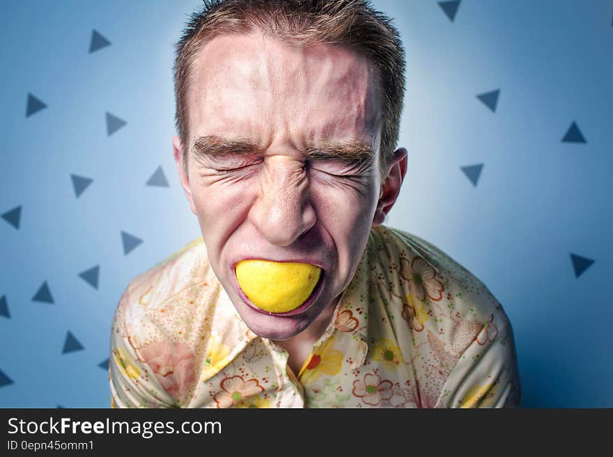 Man grimacing while eating whole lemon in studio portrait. Man grimacing while eating whole lemon in studio portrait.