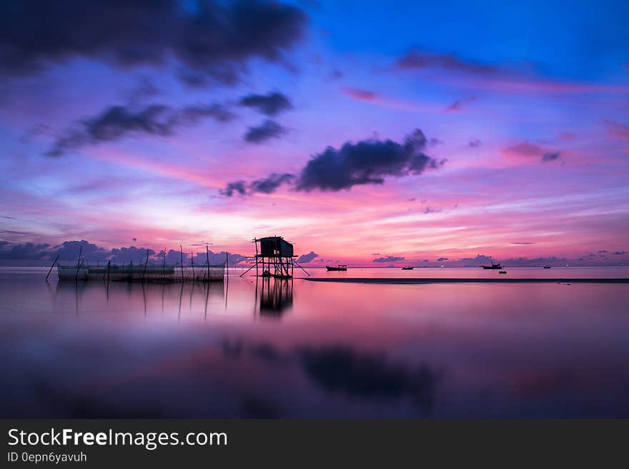 Scenic view of colorful sunset and cloudscape over tropical stilt houses on calm sea. Scenic view of colorful sunset and cloudscape over tropical stilt houses on calm sea.