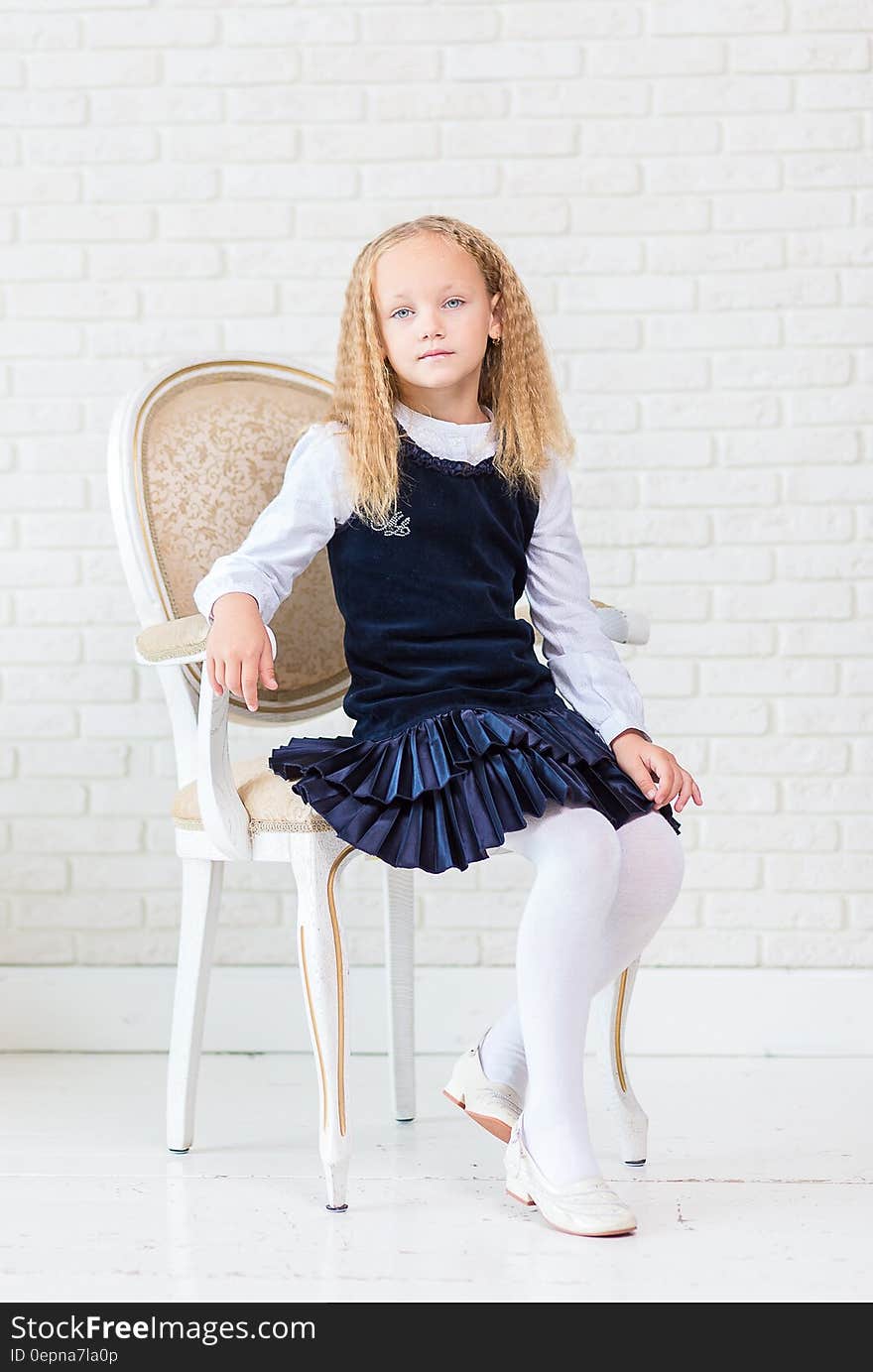 Portrait of young girl sitting in chair wearing blue dress and tights.