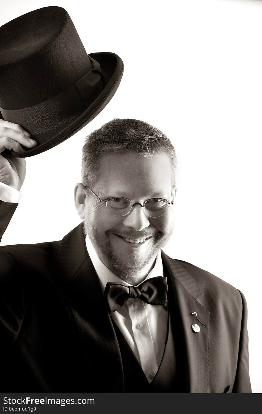 Man in Tuxedo and Eyeglasses Holding Top Hat in Grayscale