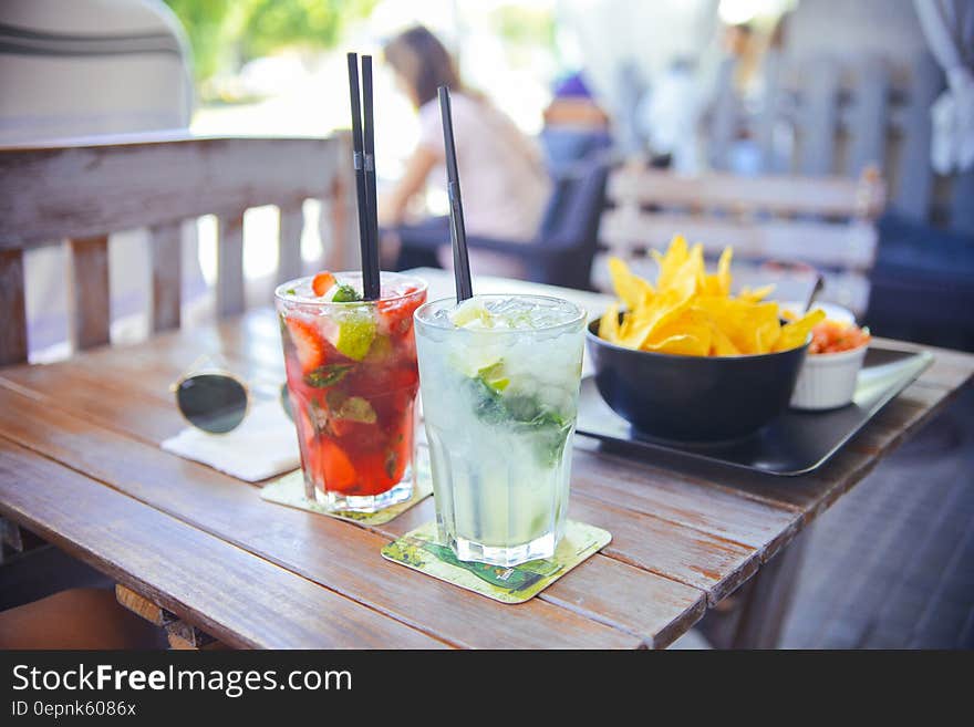 Close up of drinks and snacks on wooden outdoor table on sunny day. Close up of drinks and snacks on wooden outdoor table on sunny day.