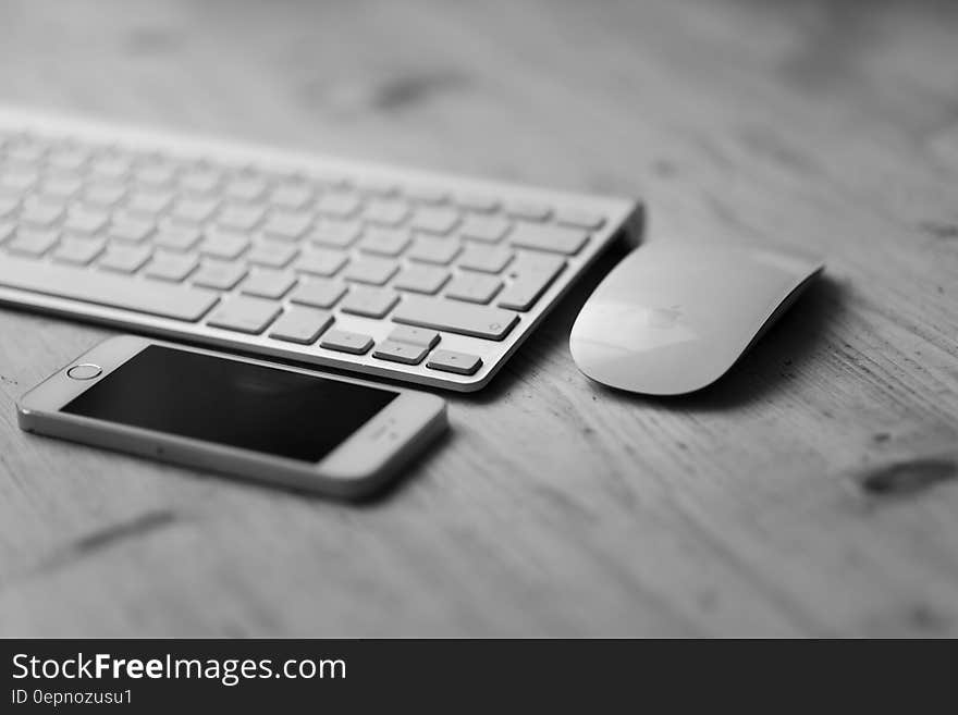 Monochrome view of white keyboard, iPhone and mouse on wooden desk. Monochrome view of white keyboard, iPhone and mouse on wooden desk.