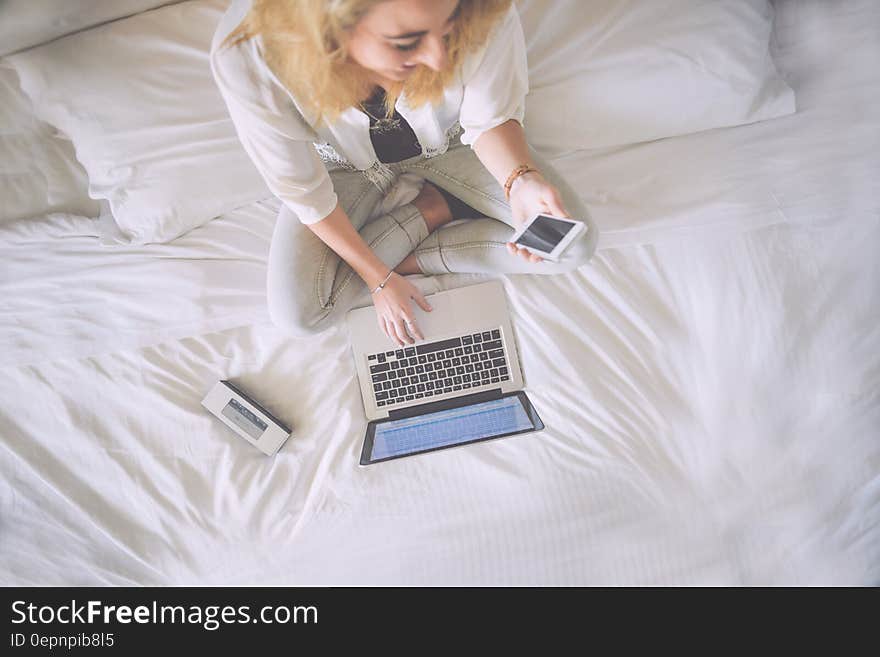 Elevated view of blond businesswoman on bed using Apple Macbook and Iphone.