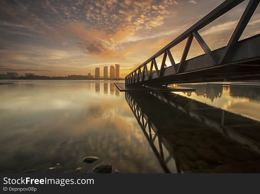 Bridge reflecting on sea at sunset with city skyline skyscrapers in background. Bridge reflecting on sea at sunset with city skyline skyscrapers in background.