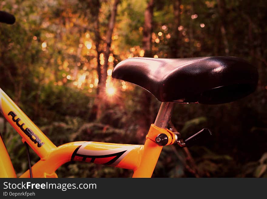 Close up of saddle on an adventure (mountain) bike with height adjustment and decorated yellow frame, background blur of trees and forest. Close up of saddle on an adventure (mountain) bike with height adjustment and decorated yellow frame, background blur of trees and forest.