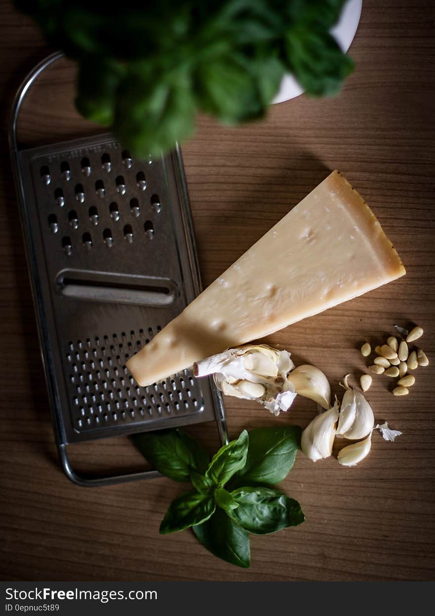 Ingredients for pesto including Parmesan cheese wedge and grater, garlic, pine nuts and fresh basil on wood. Ingredients for pesto including Parmesan cheese wedge and grater, garlic, pine nuts and fresh basil on wood.