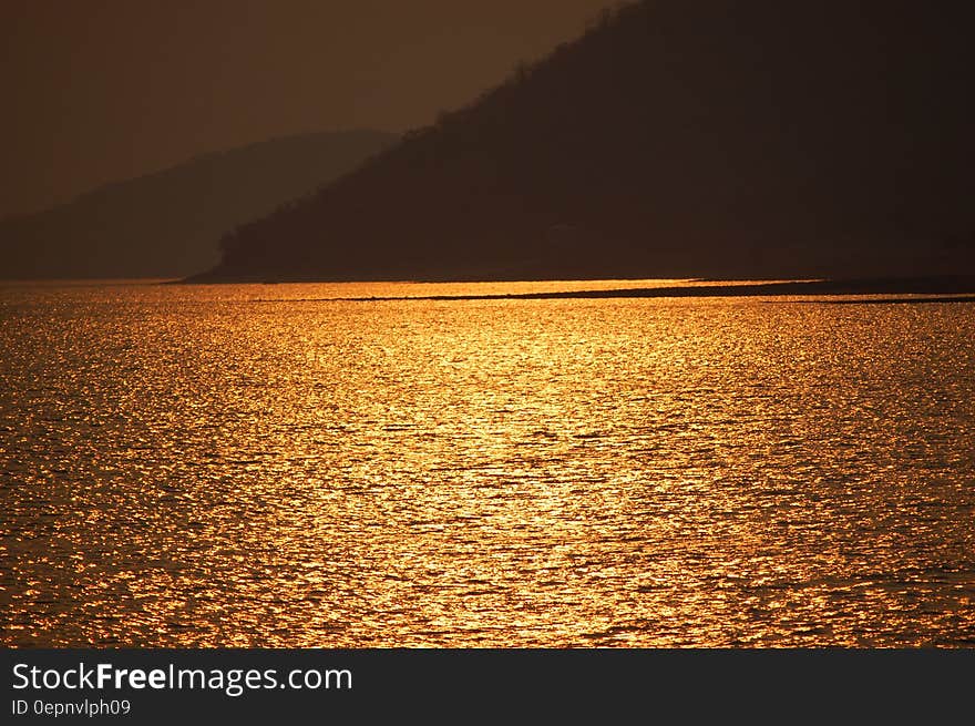 Blue Sea Near Brown Mountain during Sunset