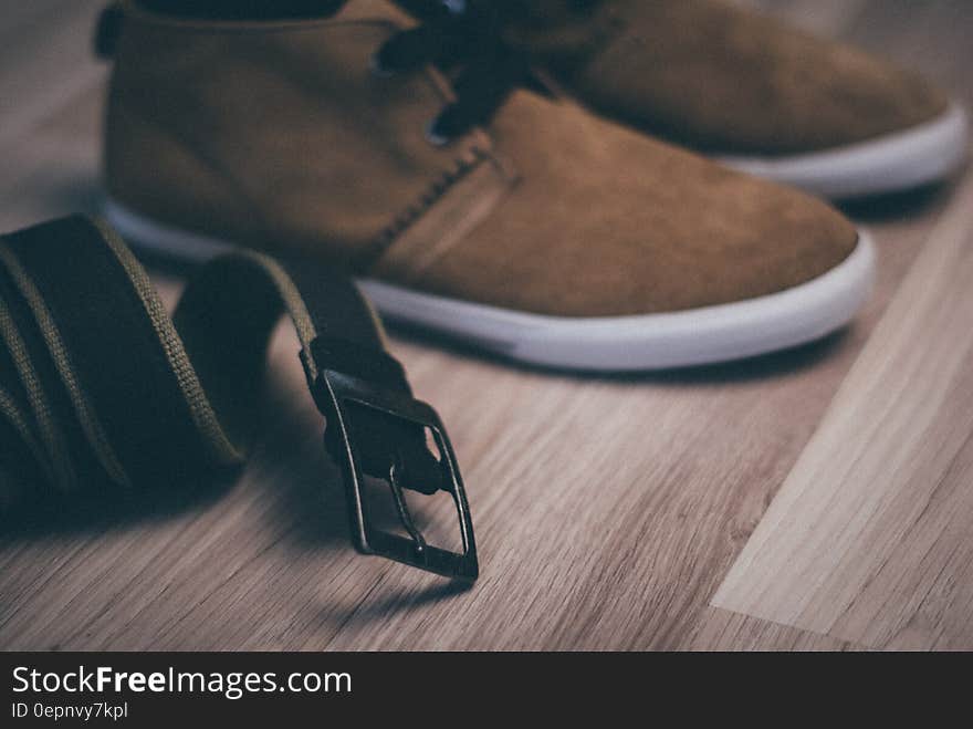 A belt next to shoes on wooden surface. A belt next to shoes on wooden surface.