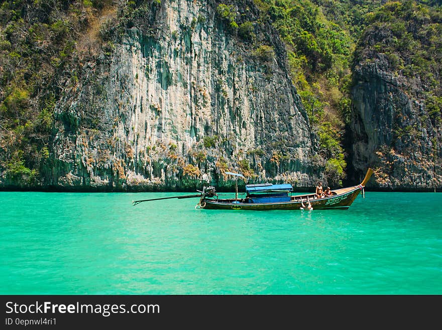 Brown Blue Boat Near Cliff and Water