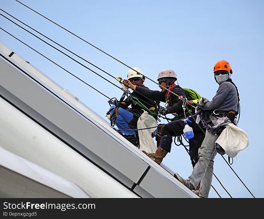 A group of workers hanging on the side of a building on safety harnesses and ropes. A group of workers hanging on the side of a building on safety harnesses and ropes.