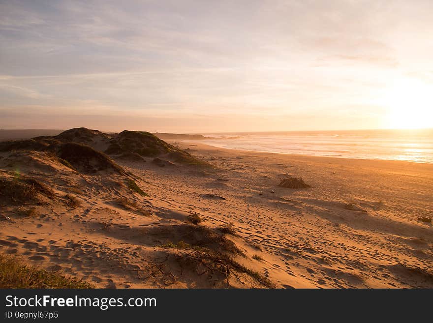 Sand dunes in desert landscape at sunset with sea in background.