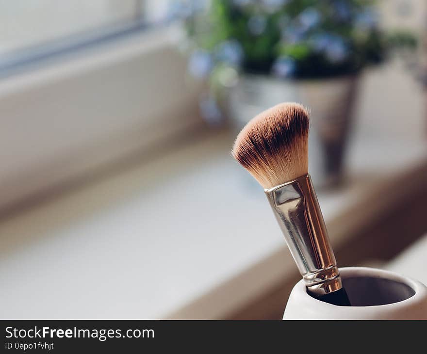 Make-up brush in cup next to sunny window.