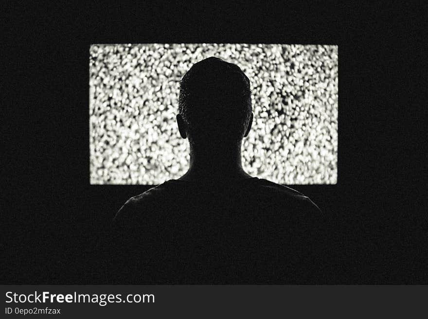 Silhouette of young man watching screen (cinema or television or computer) with noise on it; concept of wasting time instead of doing something useful. Silhouette of young man watching screen (cinema or television or computer) with noise on it; concept of wasting time instead of doing something useful.