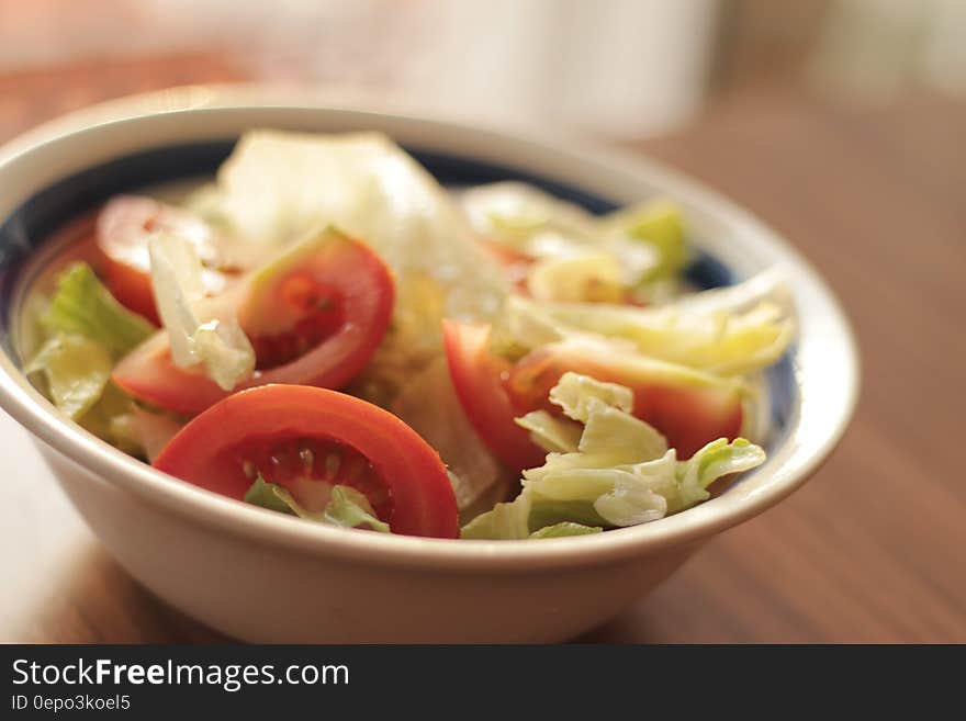 Close up of blue and white china bowl with lettuce and tomato salad on wooden table. Close up of blue and white china bowl with lettuce and tomato salad on wooden table.