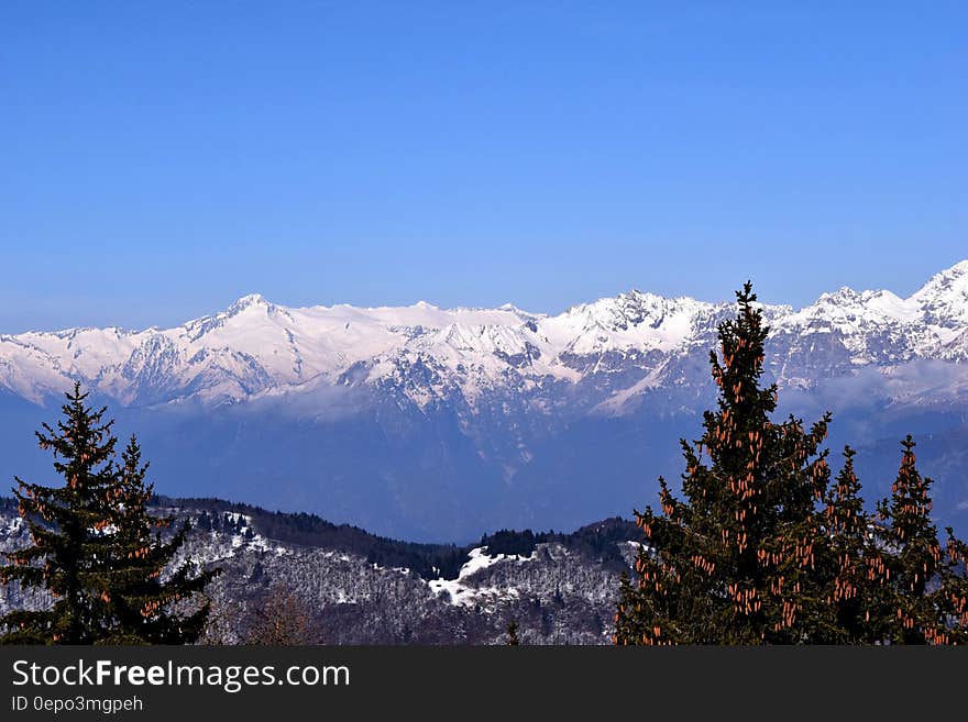 Landscape of snow covered mountain peaks over forest in valley against blue skies on sunny day. Landscape of snow covered mountain peaks over forest in valley against blue skies on sunny day.