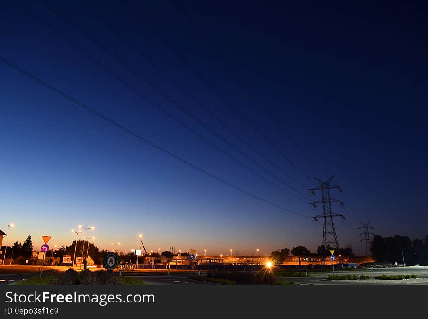 Electric stanchion and power lines along roadway illuminated at night. Electric stanchion and power lines along roadway illuminated at night.