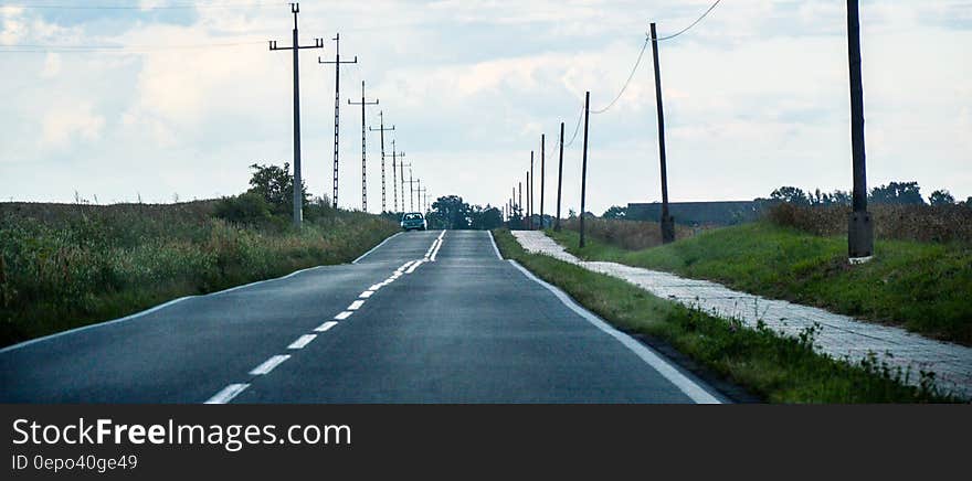 Gray Asphalt Road Between Green Grass and Gray Electric Post during Daytime