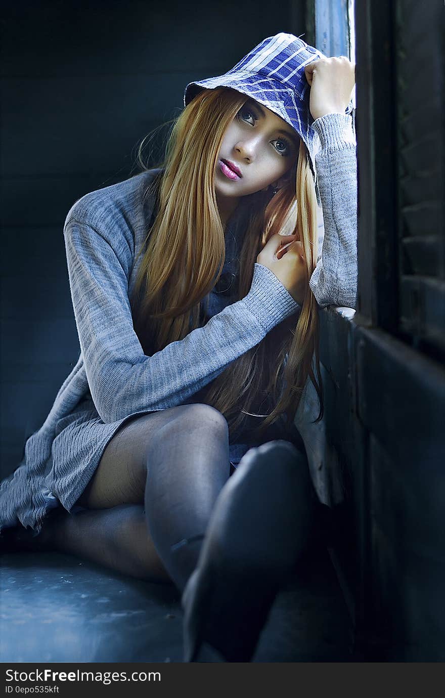 Fashion portrait of young woman in blue shirt and tights next to sunny window.