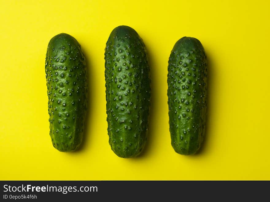 Close up of whole green cucumbers on yellow background.