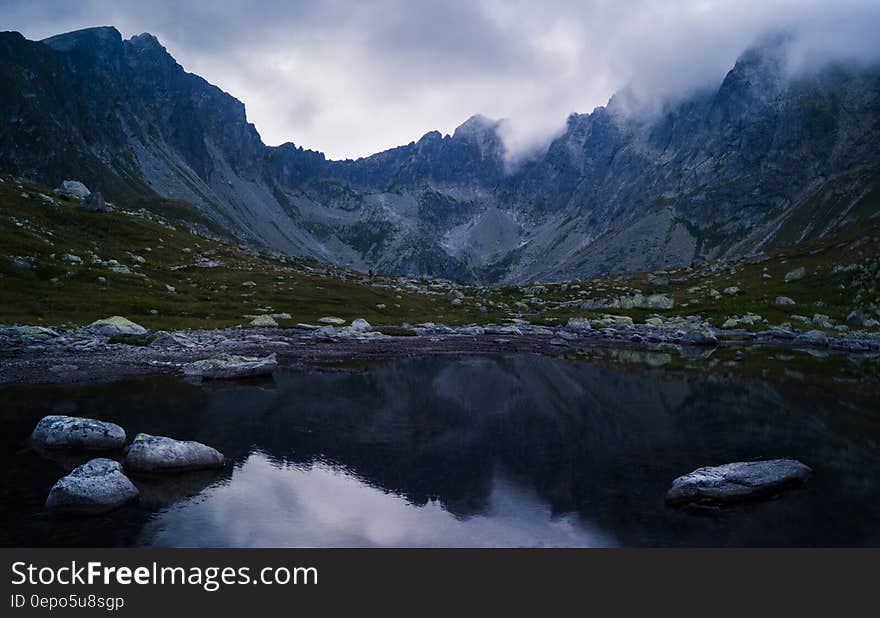 Water Besides Grey Stone Near Green Grass and Mountain during Cloudy Day