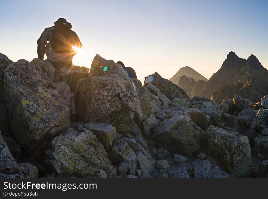 Person Sitting on Gray Rocks Under Clear Blue Sky