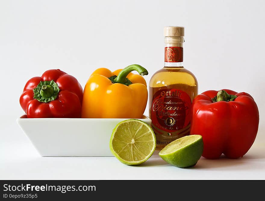 Red and Green Bell Pepper Inside White Ceramic Tray Near to Bottle and Lemon