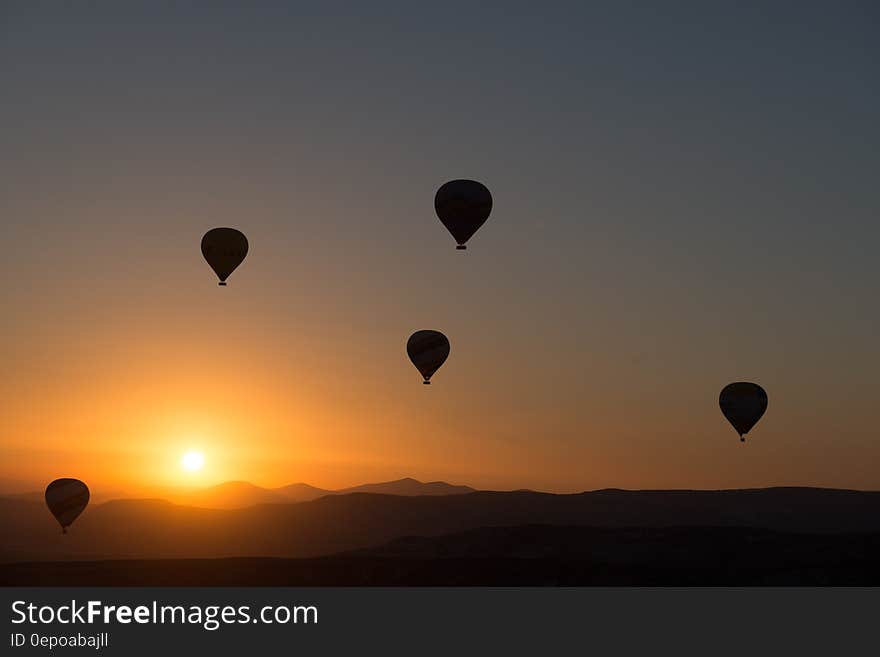 Silhouettes of hot air balloons flying over the mountains at sun rise, golden sky. Silhouettes of hot air balloons flying over the mountains at sun rise, golden sky.