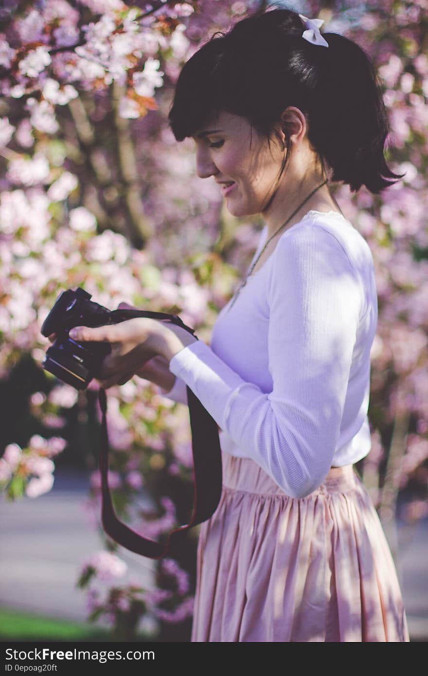 Woman in White Long Sleeve Top and Pink Skirt Holding Black Dslr Camera