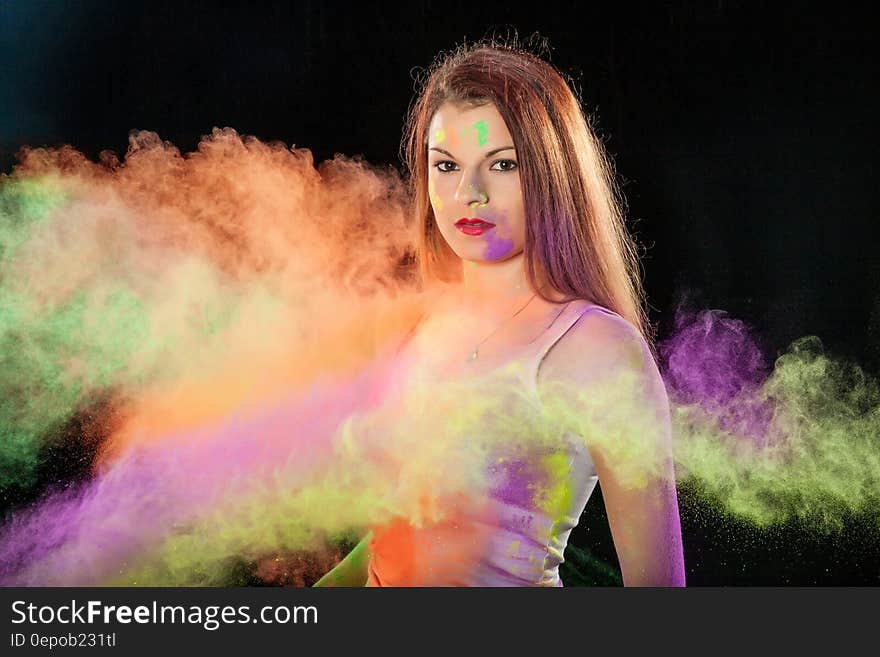 Portrait of brunette woman with purple and green smudges standing in colorful smoke. Portrait of brunette woman with purple and green smudges standing in colorful smoke.