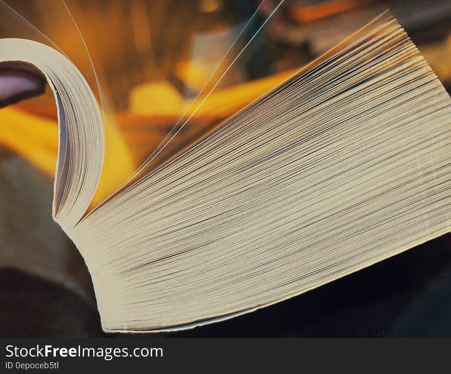 Unseen person leafing through a very thick book with binding visible, golden background.