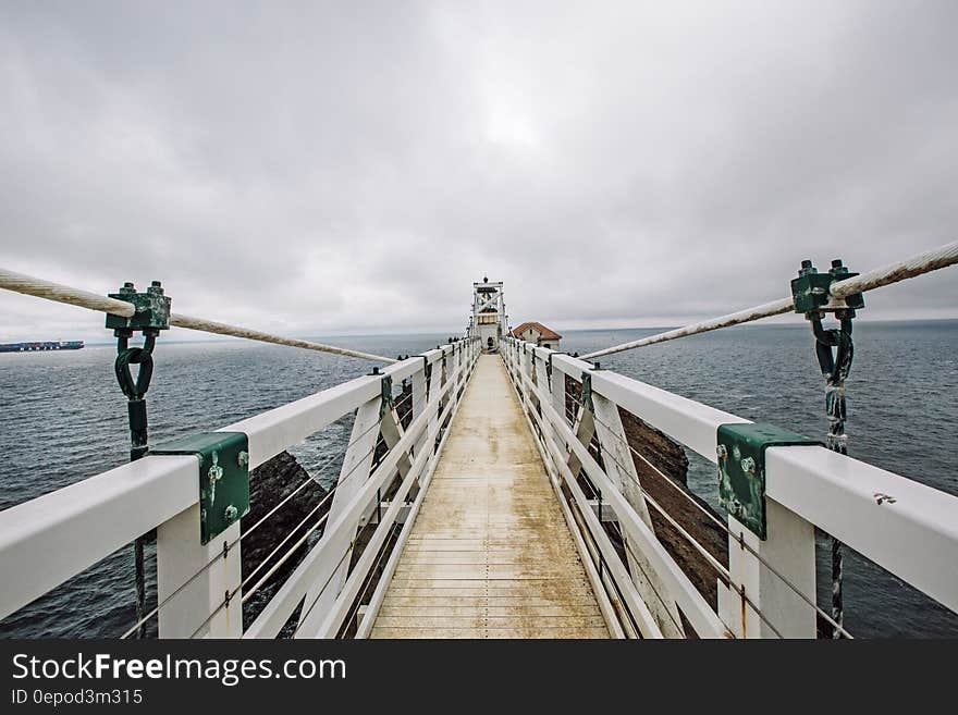 White suspension bridge with wooden planking floor showing supporting cables and safety wires, background of gray cloudy sky. White suspension bridge with wooden planking floor showing supporting cables and safety wires, background of gray cloudy sky.