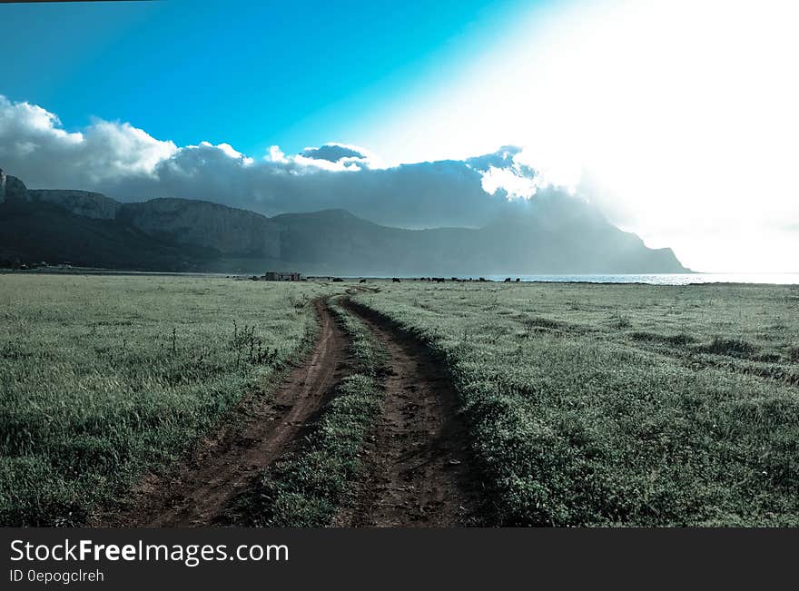 Green Grass Field Beside Brown Mountains Under White Cloudy Sky