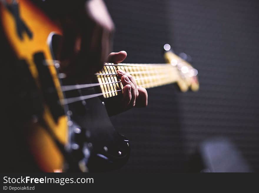 Person Playing Sun Burst Electric Bass Guitar in Bokeh Photography