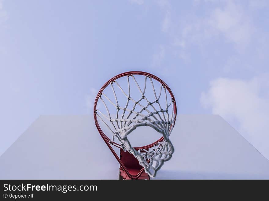 Basketball net on rim on white backboard against blue skies.