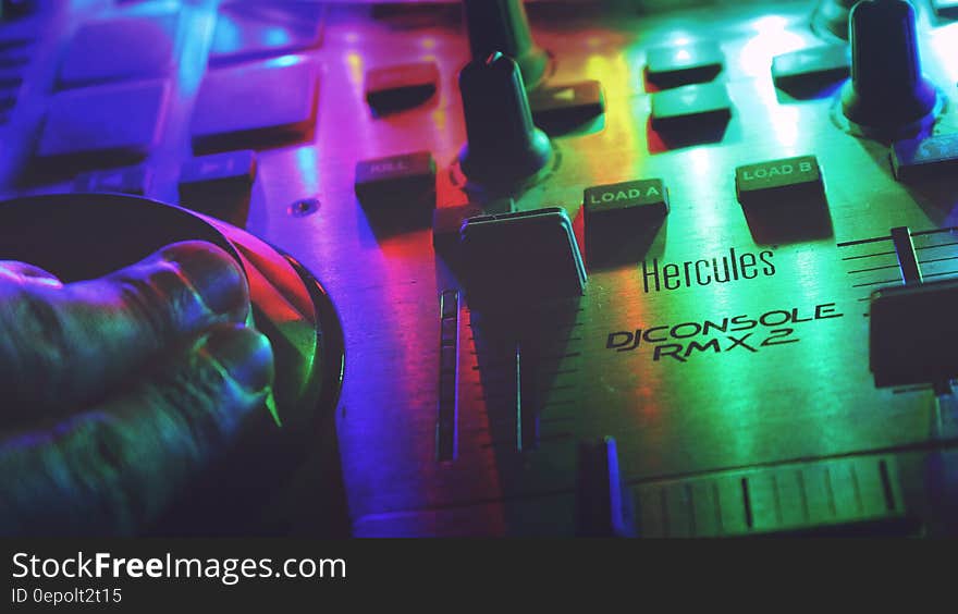 Hands on controls of close up of Hercules DJConsole RMX2 sound mixer with rainbow colors.