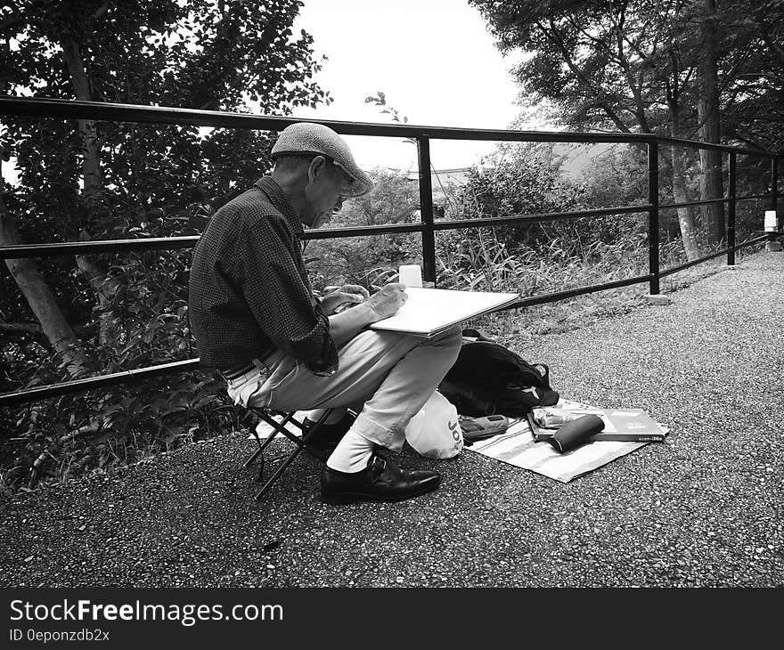 A man sketching next to a railing in the forest.