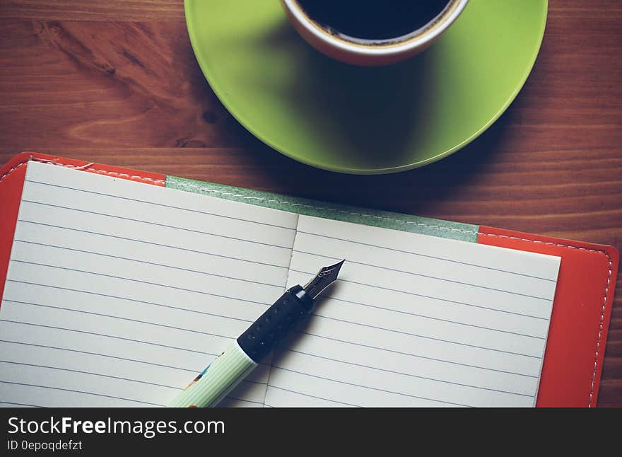 Fountain Pen on Top of Notebook Beside Drinking Mug