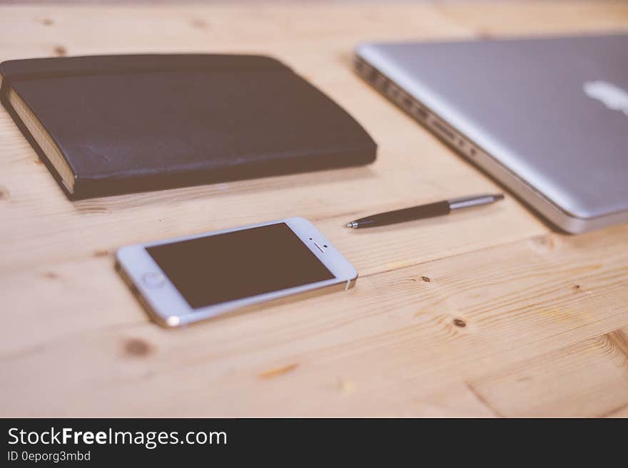 Apple notebook computer and smartphone with leather journal and pen on wooden desk. Apple notebook computer and smartphone with leather journal and pen on wooden desk.