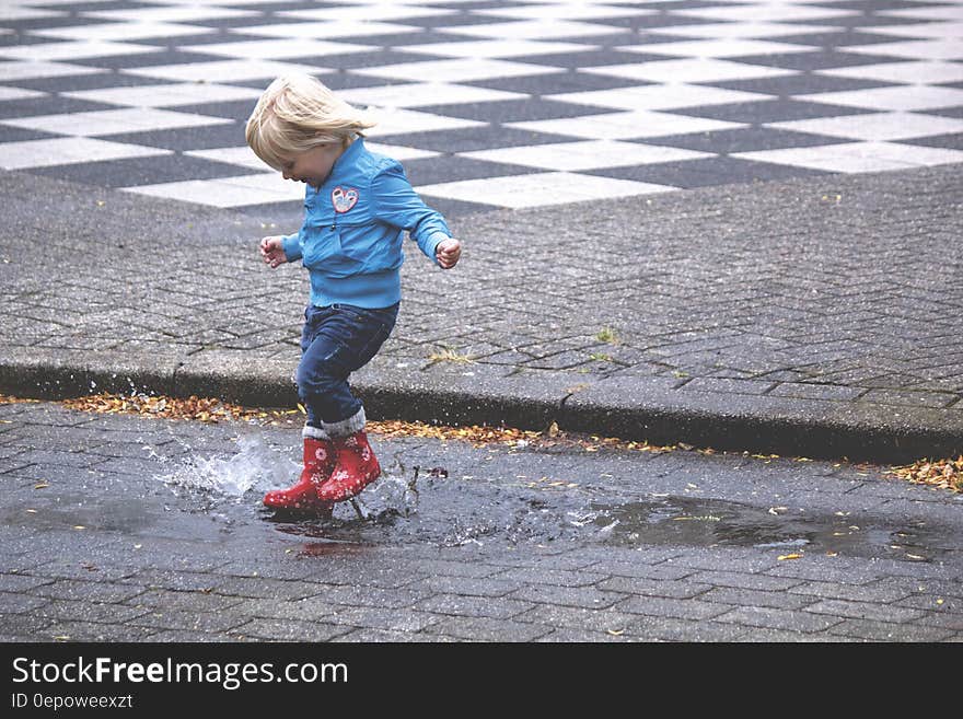 Boy in Blue Jacket Hopping on Water Puddle