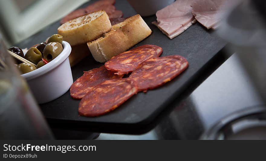 Tray of appetizing foods including green olives, bread, ham and salami.