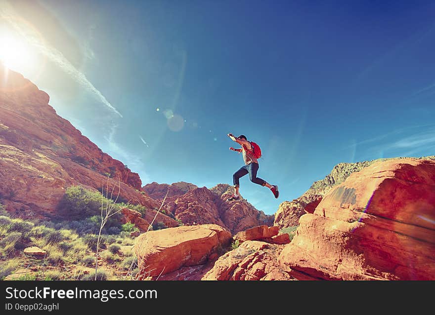 Man with backpack jumping over rocks in desert landscape on sunny day. Man with backpack jumping over rocks in desert landscape on sunny day.