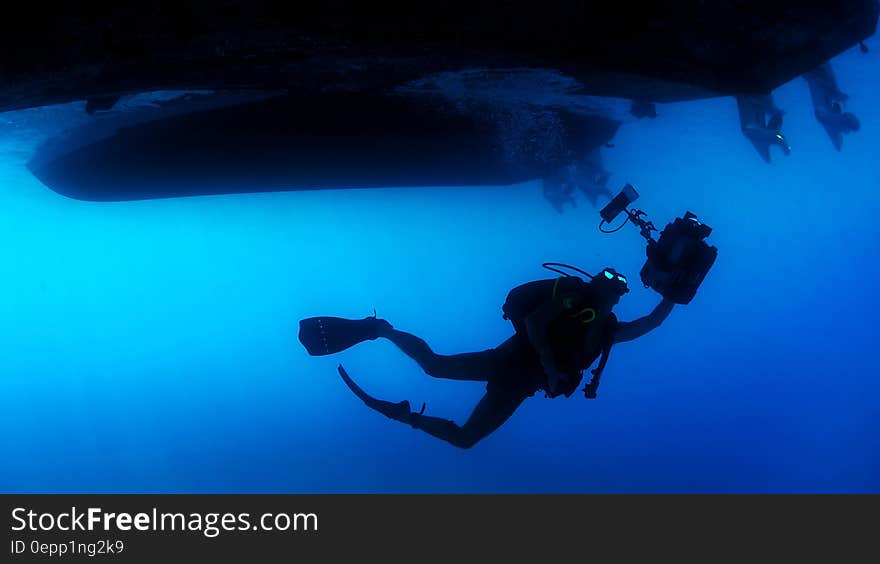 Scuba diver with equipment under ship in blue waters. Scuba diver with equipment under ship in blue waters.