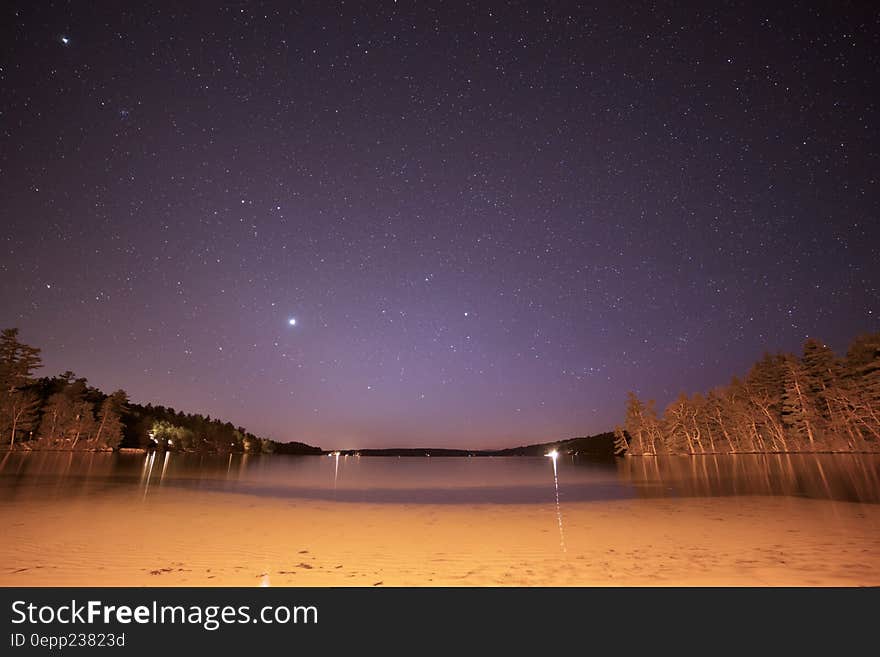 Stars in night skies over sandy beach on waterfront.