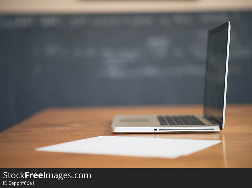 Laptop computer open on wooden school desk with paper against blackboard inside classroom. Laptop computer open on wooden school desk with paper against blackboard inside classroom.