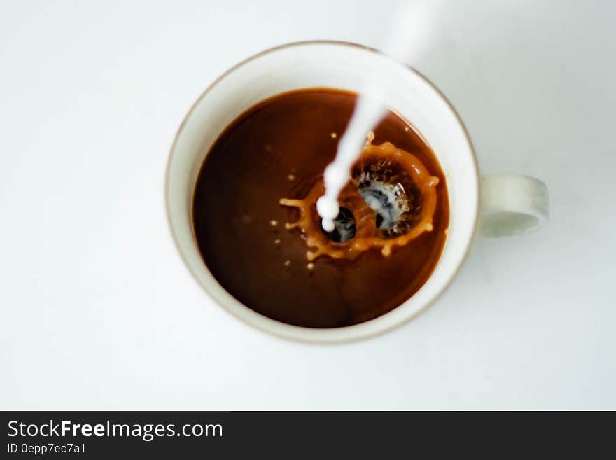 Overhead of milk pouring and splashing into cup of coffee. Overhead of milk pouring and splashing into cup of coffee.