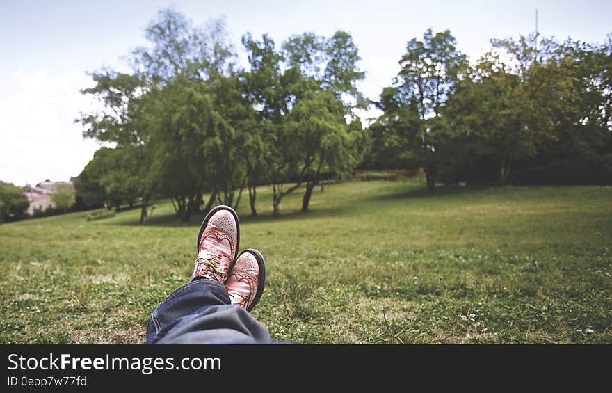 Person Lying on Grass Field Near Trees Under White Clouds during Daytime